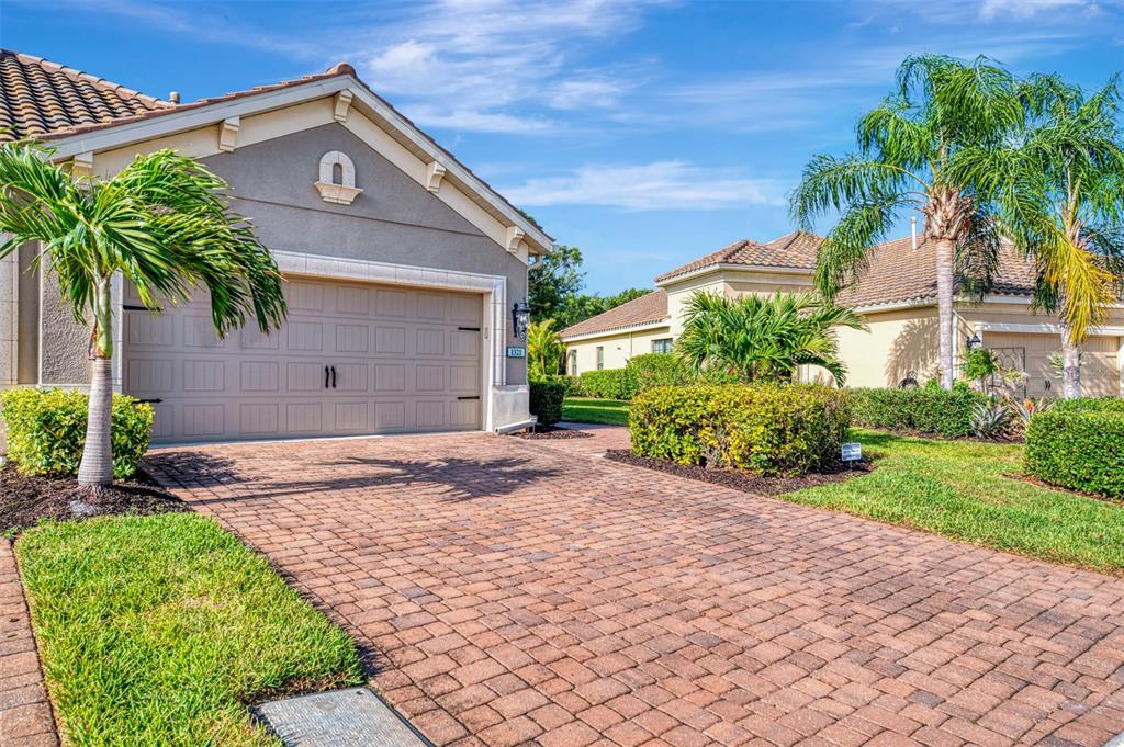 A beige house with a brick paver driveway and palm trees under a blue sky — 1321 BACKSPIN DRIVE, ENGLEWOOD, FL