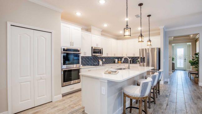A modern kitchen features white cabinets, a large island with bar seating, and stainless appliances — 8646 OAKSTONE CIRCLE, LEESBURG, FL