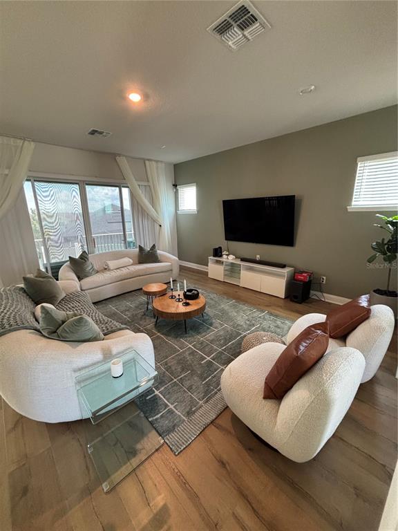 A living room features light wood floors, a large area rug, and modern white furniture — 13186 MAGNOLIA VALLEY DRIVE, CLERMONT, FL