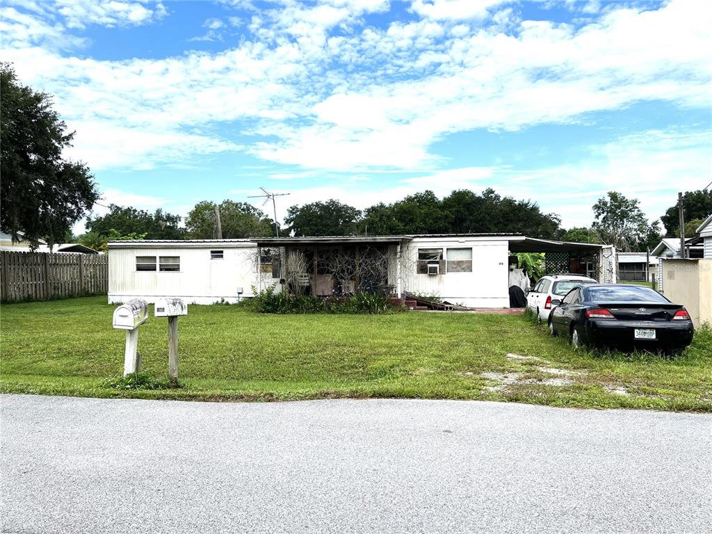 A single-story mobile home with a front porch sits on a grassy lot with cars — 170 N OAK DRIVE, KENANSVILLE, FL
