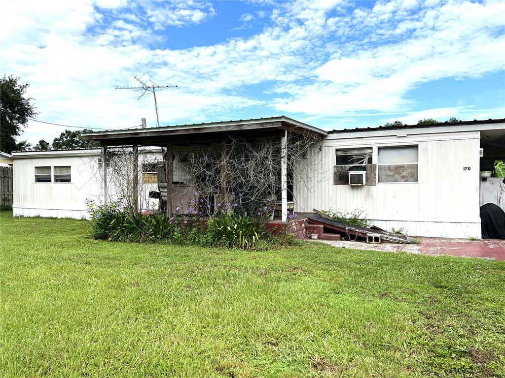 A single-story mobile home with a covered porch and a grassy yard under a cloudy sky — 170 N OAK DRIVE, KENANSVILLE, FL