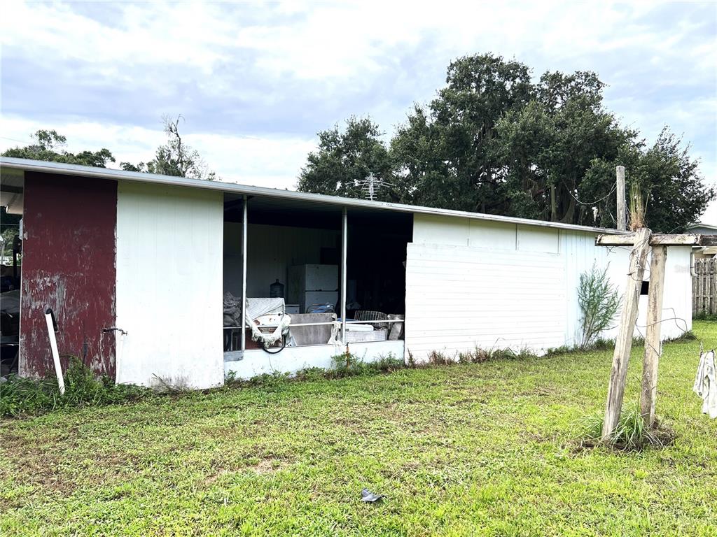 A white exterior wall features a large open-air porch area with stored items inside — 170 N OAK DRIVE, KENANSVILLE, FL