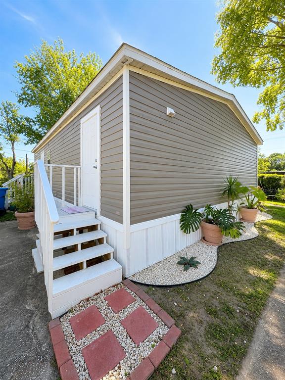 The exterior of a mobile home features tan siding, white stairs, and a landscaped garden bed — 1111 AVENUE G, ORMOND BEACH, FL