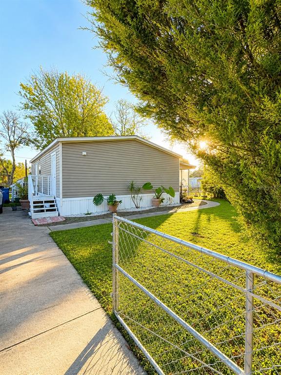 A side view of a tan mobile home with a white staircase and chain-link fence — 1111 AVENUE G, ORMOND BEACH, FL