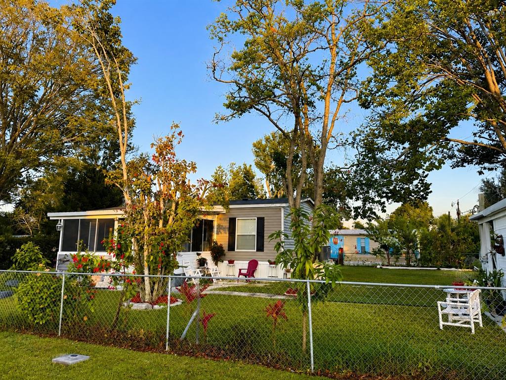 A single-story manufactured home with a screened porch sits behind a chain-link fence — 1111 AVENUE G, ORMOND BEACH, FL