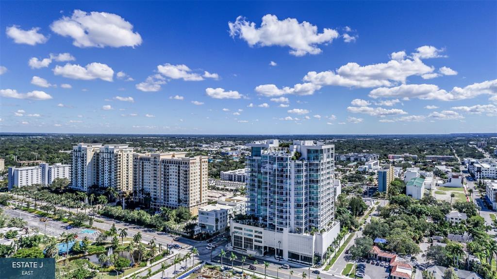 An aerial view shows a modern high-rise building surrounded by other residential structures and trees — 555 QUAY COMMONS UNIT 1704, SARASOTA, FL