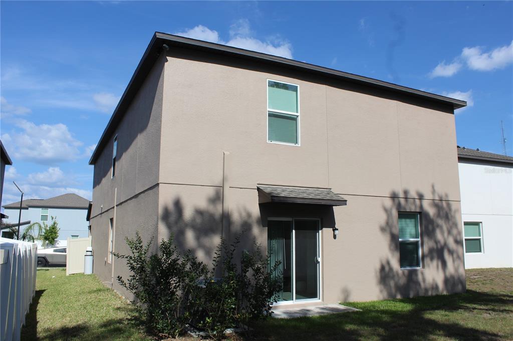 The exterior rear view of a two-story tan stucco house with a sliding glass door — 6259 BACK FORTY LOOP, ZEPHYRHILLS, FL