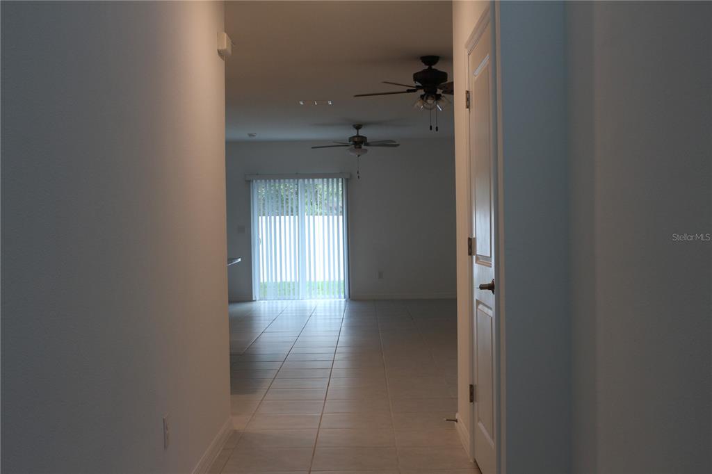 A hallway with tile flooring leads to a living area with sliding glass doors — 6259 BACK FORTY LOOP, ZEPHYRHILLS, FL