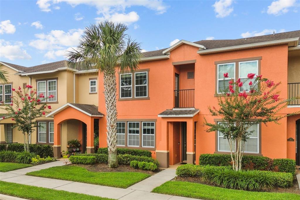 A two-story orange stucco townhouse with a palm tree and flowering bushes in the front — 561 TELFAIR SQUARE COURT, SANFORD, FL