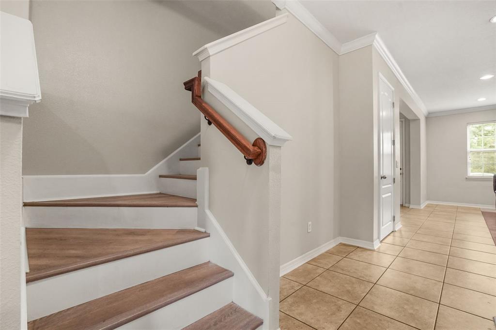 A staircase with wood-look treads and a wooden handrail sits beside a tiled hallway — 561 TELFAIR SQUARE COURT, SANFORD, FL