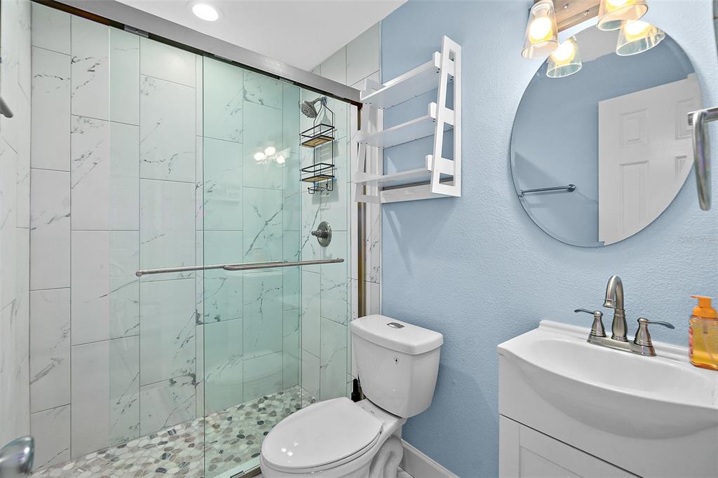 A bathroom features a glass-enclosed shower with marble-look tile, a toilet, and a vanity sink — 300 S CENTRAL AVENUE UNIT 203, FLAGLER BEACH, FL