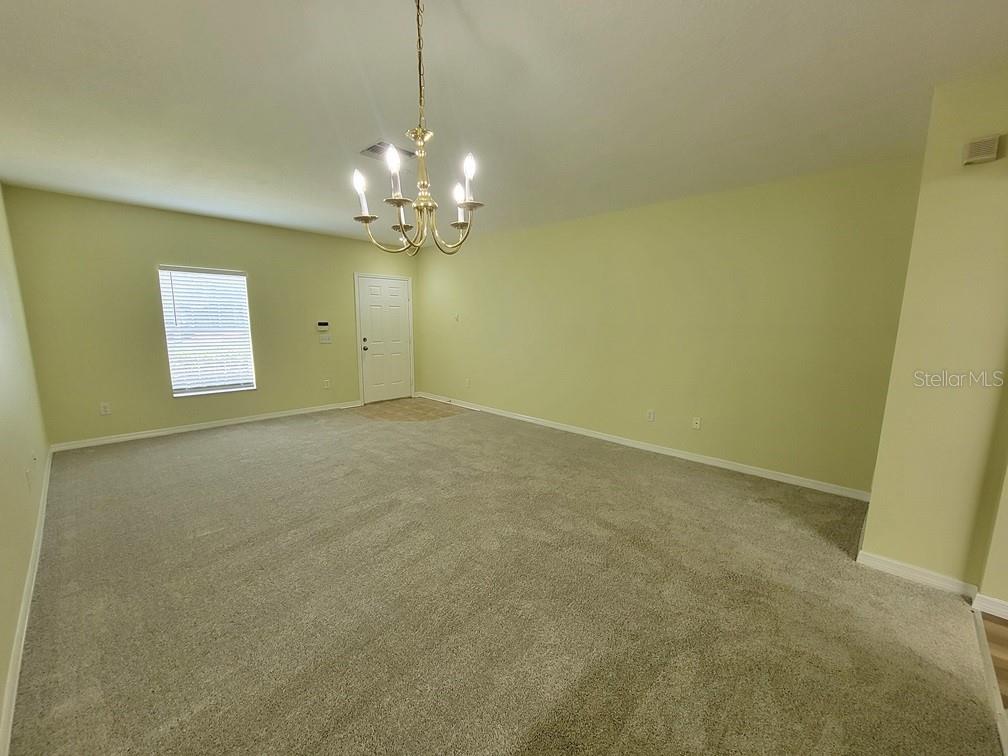 An empty room features beige carpeting, light green walls, and a brass chandelier — 16414 SWAN VIEW CIRCLE, ODESSA, FL