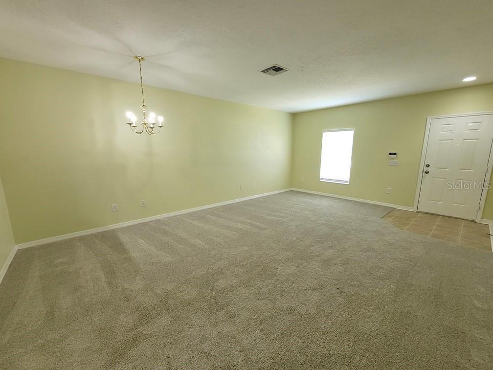 An empty living room features light green walls, beige carpeting, a chandelier, and a front door — 16414 SWAN VIEW CIRCLE, ODESSA, FL