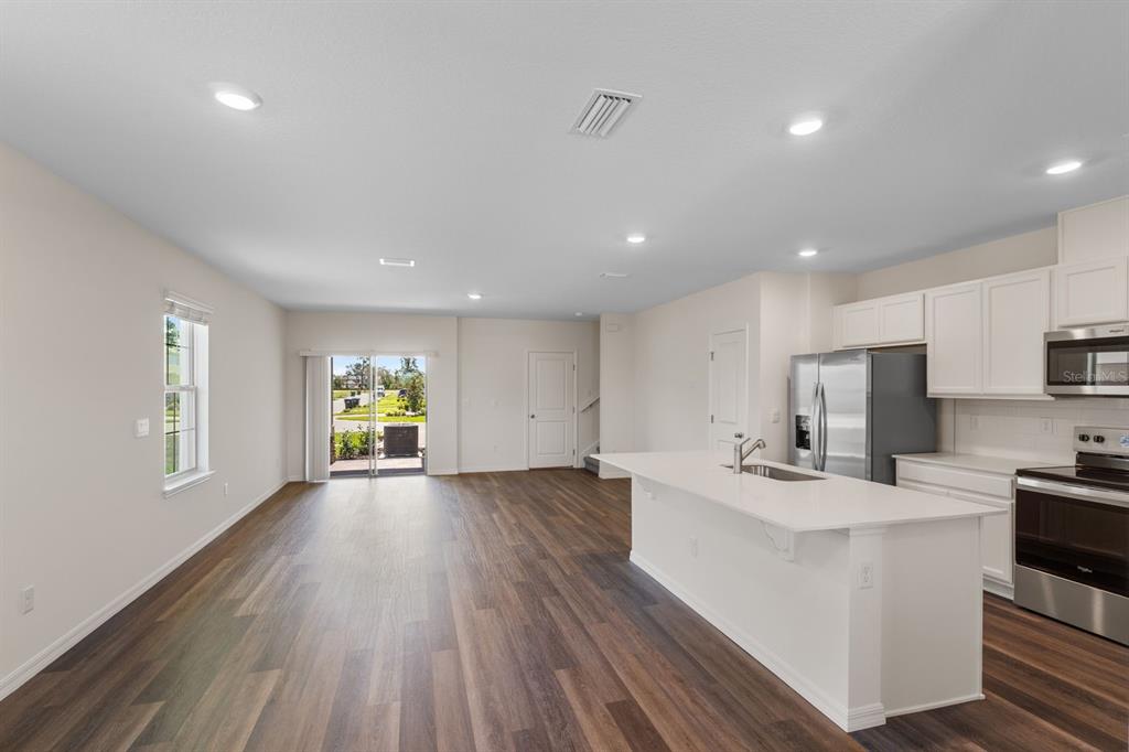 An open-concept kitchen and living area with white cabinets, stainless appliances, and wood-look flooring — 12086 SHINE VIEW LANE, WINTER GARDEN, FL