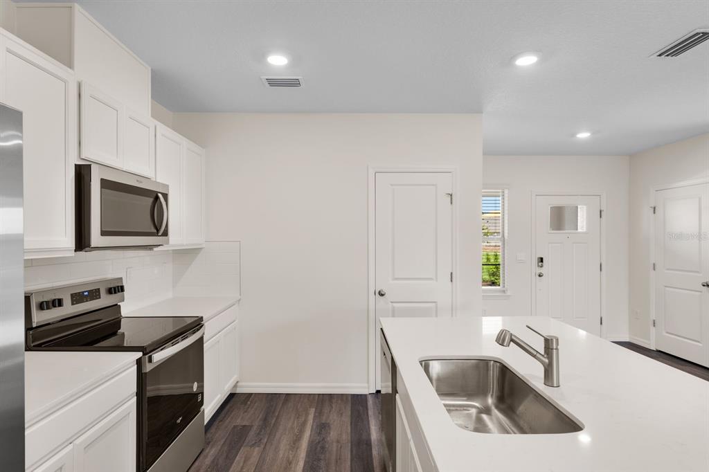 A modern kitchen features white cabinetry, stainless steel appliances, a center island, and wood flooring — 12086 SHINE VIEW LANE, WINTER GARDEN, FL