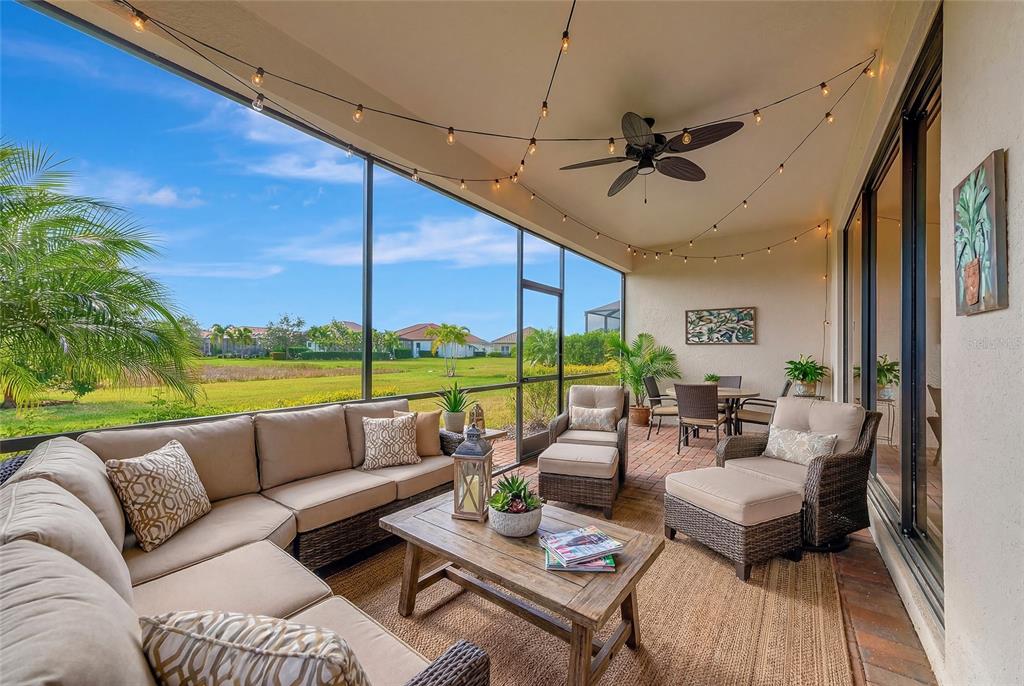 A screened-in patio features wicker furniture, a ceiling fan, string lights, and a grassy view — 10202 MARBELLA DRIVE, BRADENTON, FL