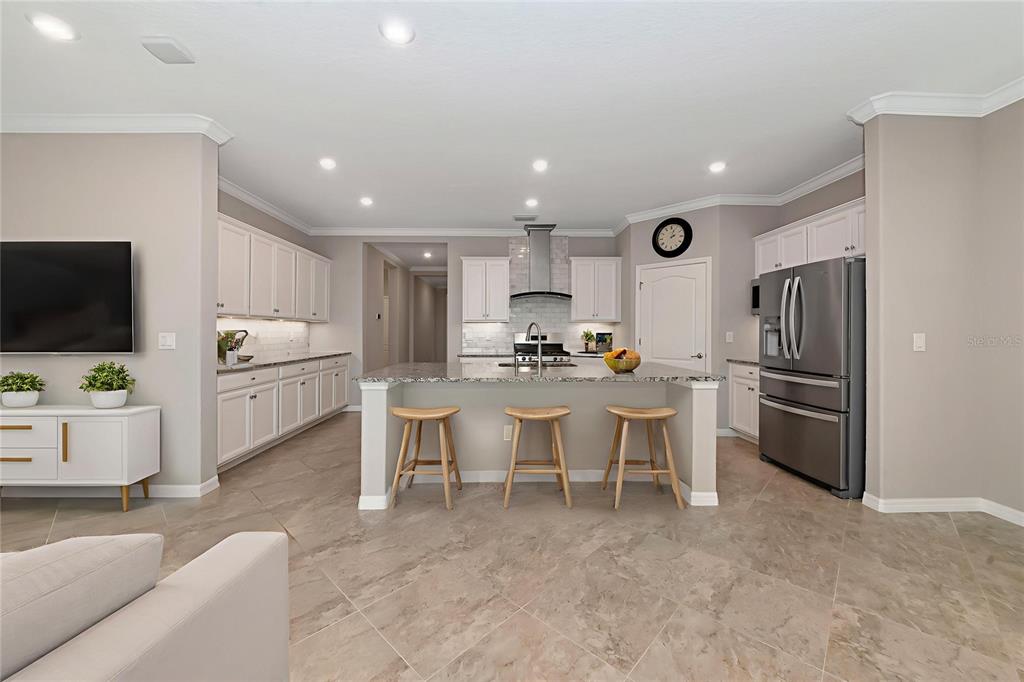 A modern kitchen features white cabinetry, a granite-topped island with three stools, and tile flooring — 10202 MARBELLA DRIVE, BRADENTON, FL