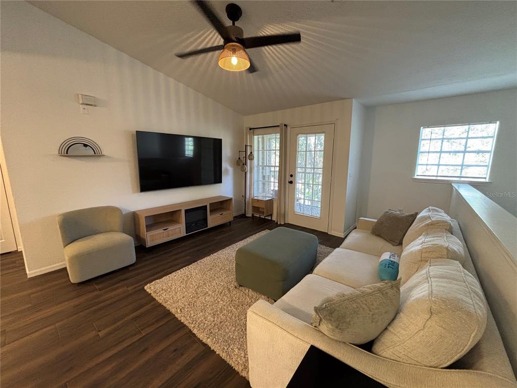 A living room features a large television, a light-colored sofa, and wood-look flooring — 8809 MANOR LOOP UNIT 202, LAKEWOOD RANCH, FL