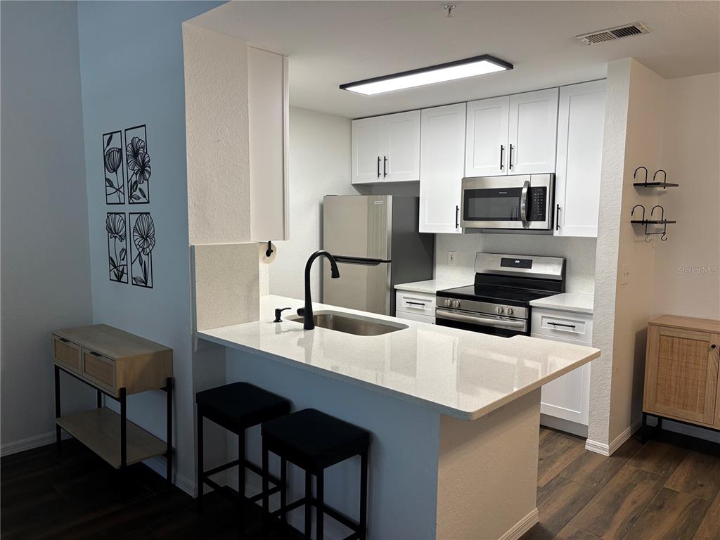 A modern kitchen features white cabinetry, stainless steel appliances, and a breakfast bar with stools — 8809 MANOR LOOP UNIT 202, LAKEWOOD RANCH, FL