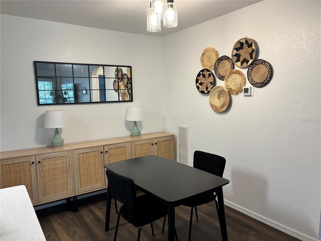 A dining area features a black table, two chairs, a wooden sideboard, and wall decor — 8809 MANOR LOOP UNIT 202, LAKEWOOD RANCH, FL