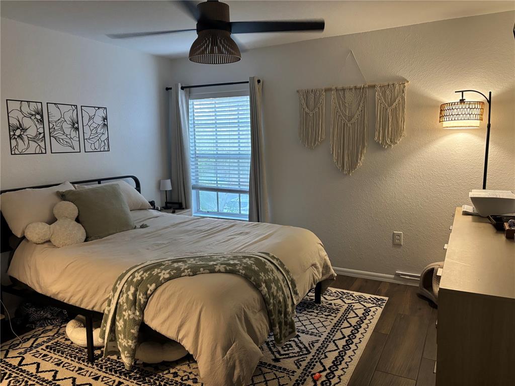 A bedroom features a bed with a patterned rug, macramé wall art, and a ceiling fan — 8809 MANOR LOOP UNIT 202, LAKEWOOD RANCH, FL