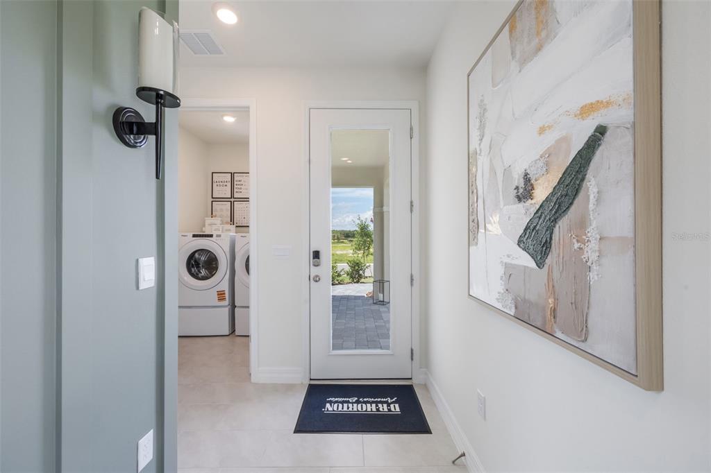 A hallway features a glass-paneled door, a laundry room entrance, and a large abstract painting — 3945 KENNEBUNK LOOP, MOUNT DORA, FL