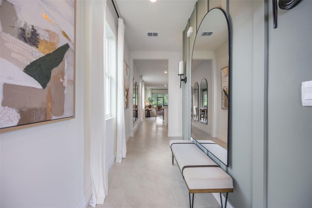 A hallway features a light-colored bench, a large arched mirror, and tile flooring — 3945 KENNEBUNK LOOP, MOUNT DORA, FL