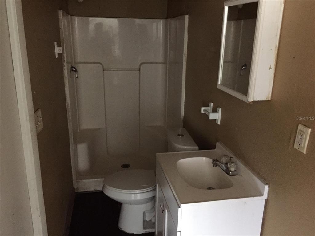 A small bathroom features a white vanity, a toilet, and a shower stall with white walls — 1489 GROTHE STREET, JACKSONVILLE, FL