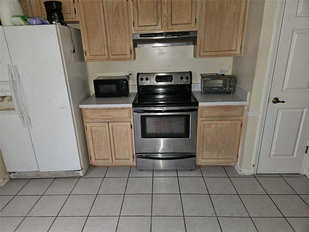 A kitchen features light wood cabinets, stainless steel appliances, and white tile flooring — 8033 MACDOUGALL DRIVE E, JACKSONVILLE, FL