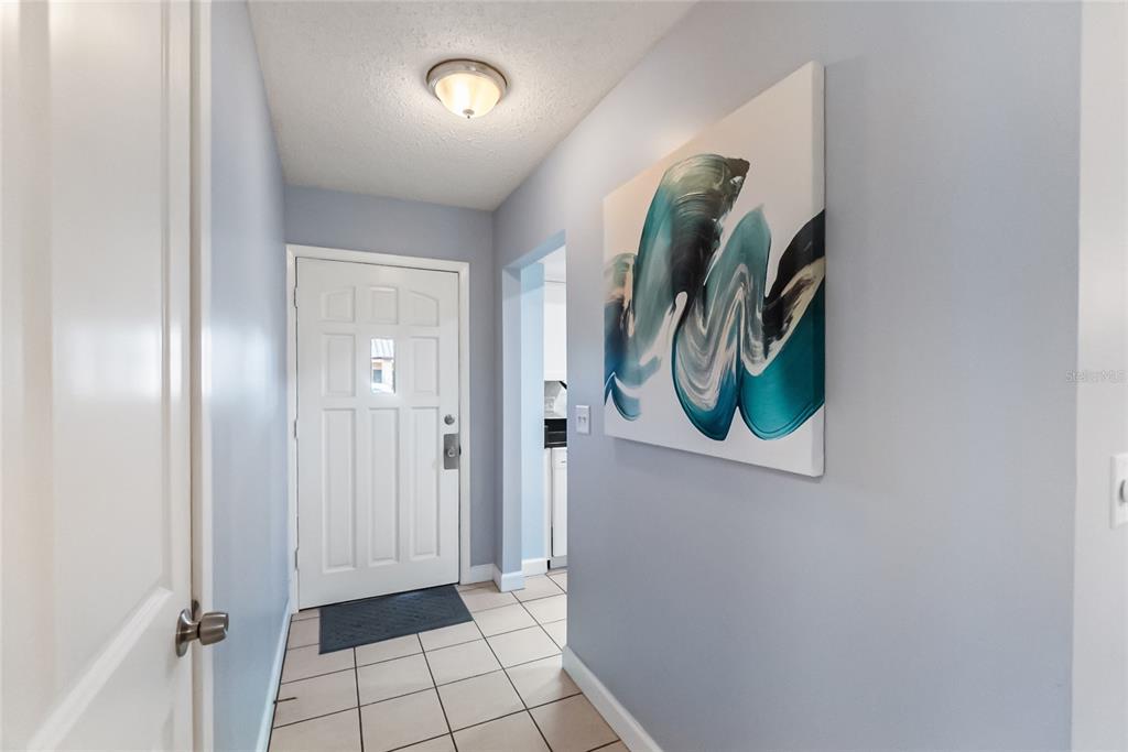A hallway features light blue walls, tile flooring, a white front door, and abstract wall art — 676 PARK CIRCLE, BRADENTON, FL