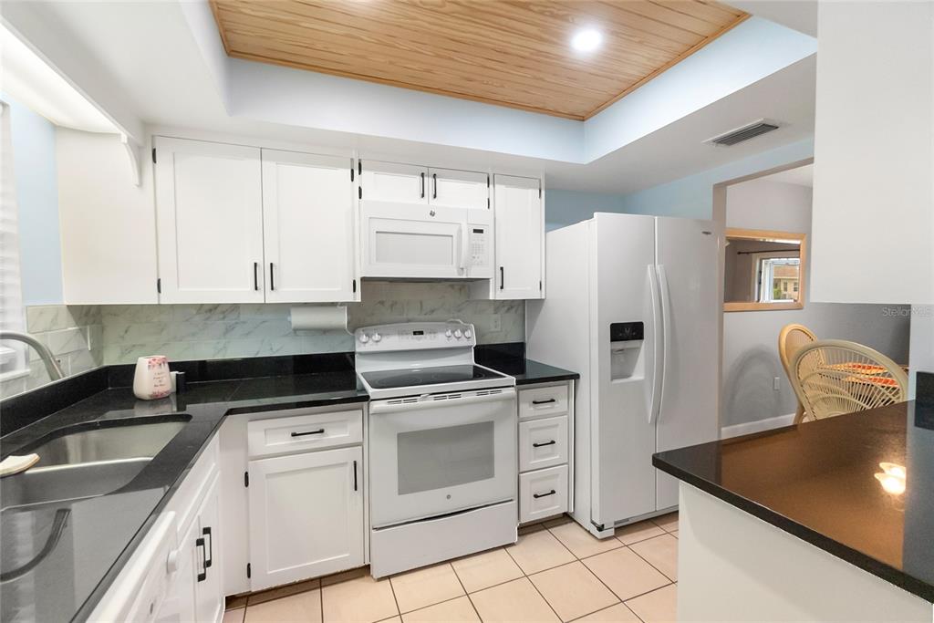 A kitchen features white cabinets, black countertops, white appliances, and a wood-paneled tray ceiling — 676 PARK CIRCLE, BRADENTON, FL