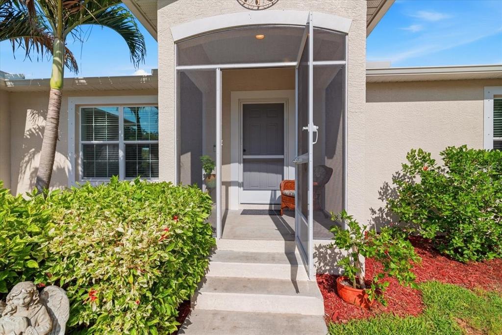 A front entryway features a screen door, concrete steps, and landscaping under a clear sky — 6143 STURGIS STREET, ENGLEWOOD, FL