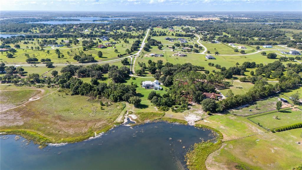 An aerial view shows a house situated on a large, grassy lot beside a lake — 19415 VILLA CITY ROAD, GROVELAND, FL