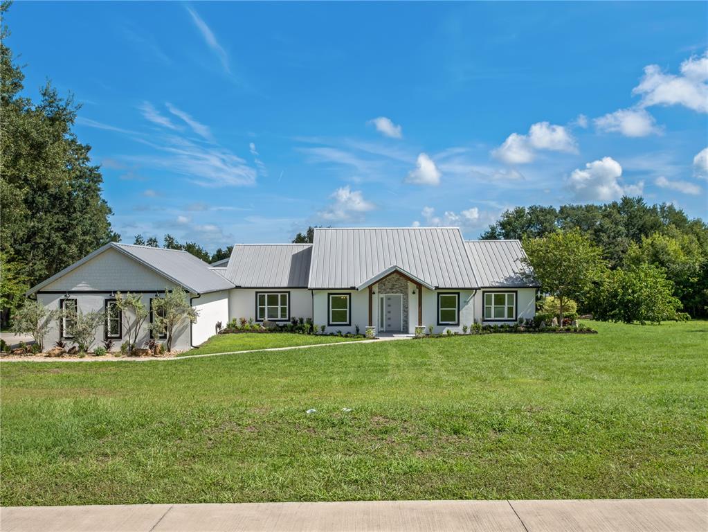 A single-story house with a metal roof, white exterior, and dark-framed windows sits on grass — 19415 VILLA CITY ROAD, GROVELAND, FL