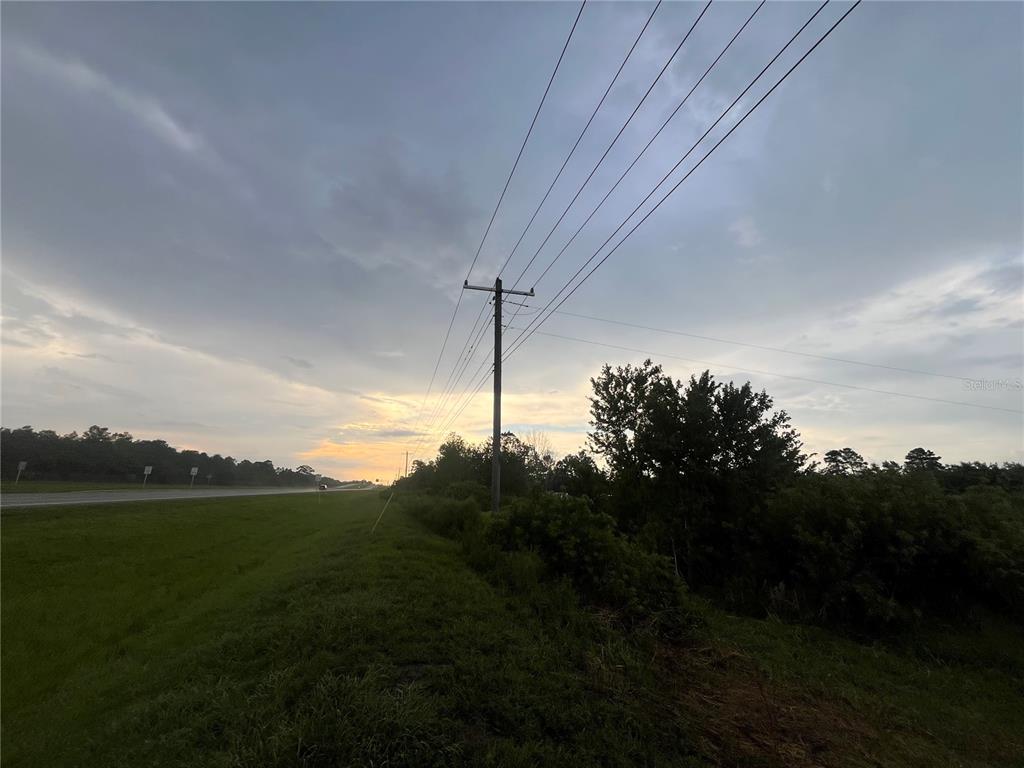A utility pole stands beside a grassy roadside under a cloudy sky at sunset — E STATE RD 60, OKEECHOBEE, FL