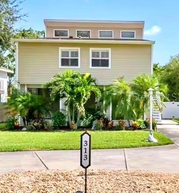 A two-story house with beige siding, palm trees, and an exterior staircase leading to a deck — 313 CRYSTAL BEACH AVENUE, CRYSTAL BEACH, FL