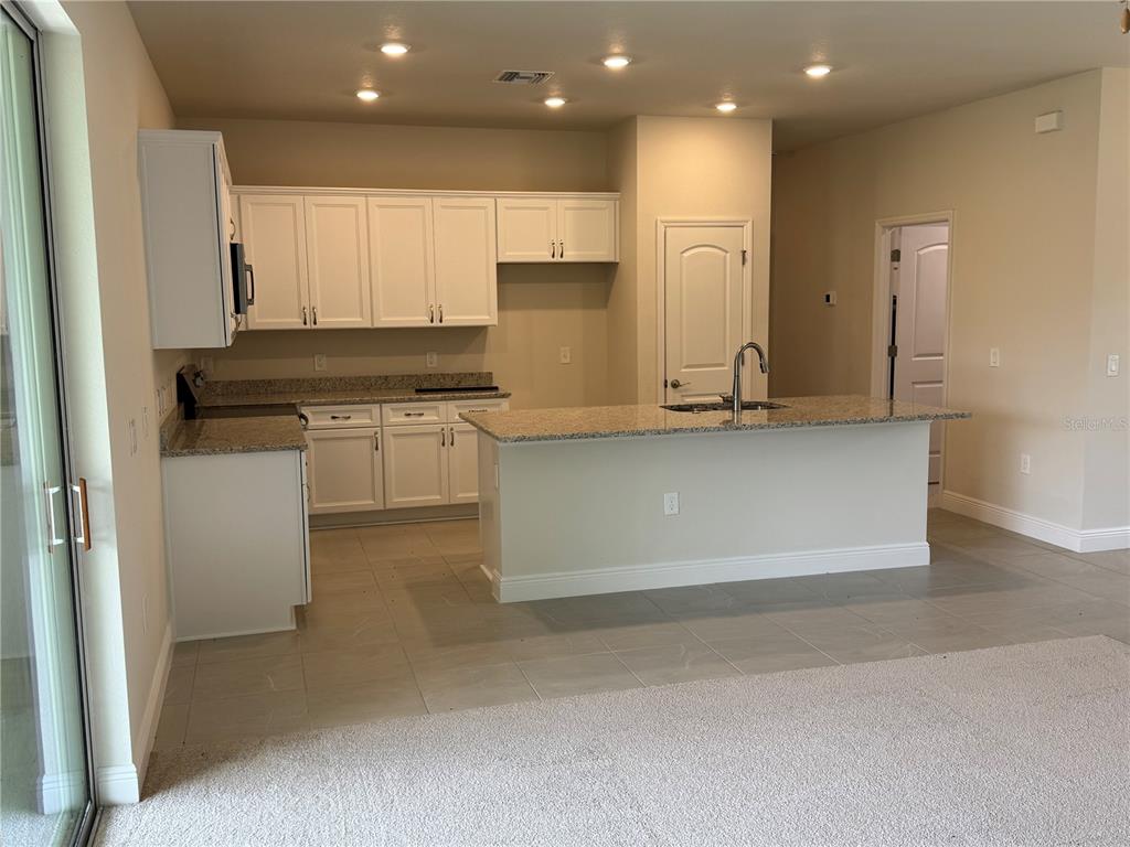 A kitchen features white cabinets, granite countertops, a center island, and tile flooring — 5874 FERENDINA STREET, NORTH PORT, FL