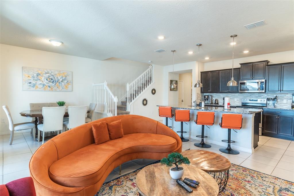 An open-concept living room and kitchen featuring an orange curved sofa and breakfast bar — 3713 PACIFIC LANE, DAVENPORT, FL