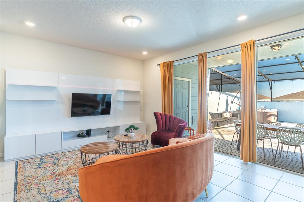 A living room features a white media wall, orange sofa, purple chair, and sliding glass doors — 3713 PACIFIC LANE, DAVENPORT, FL