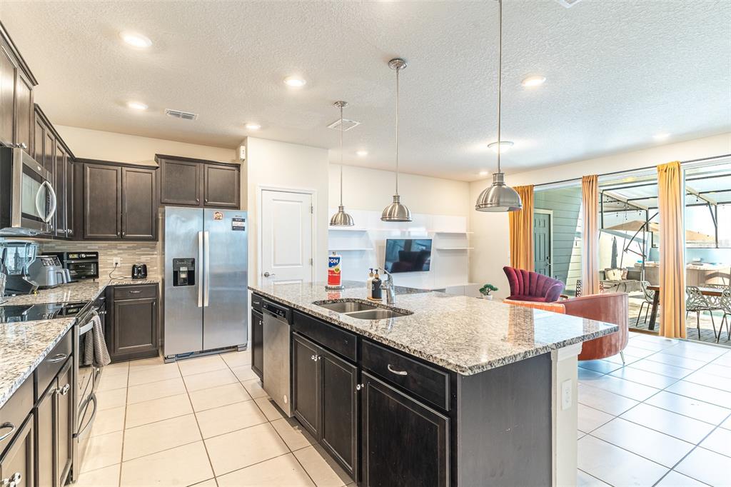 A kitchen with dark cabinets, granite countertops, and a large island opens to a living area — 3713 PACIFIC LANE, DAVENPORT, FL