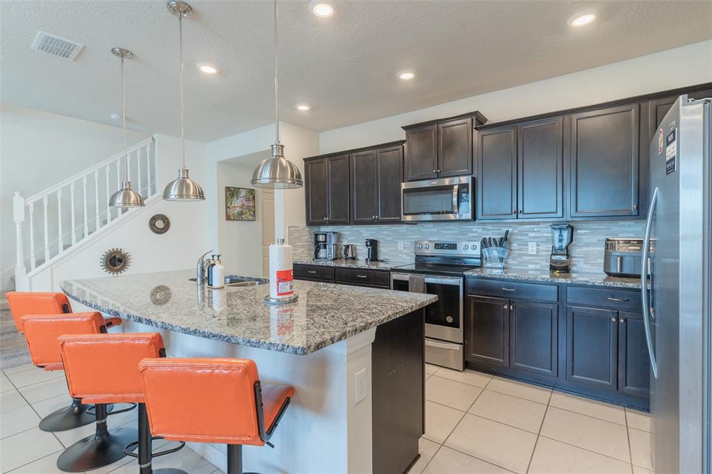 A kitchen with dark cabinets, granite countertops, stainless steel appliances, and orange bar stools — 3713 PACIFIC LANE, DAVENPORT, FL