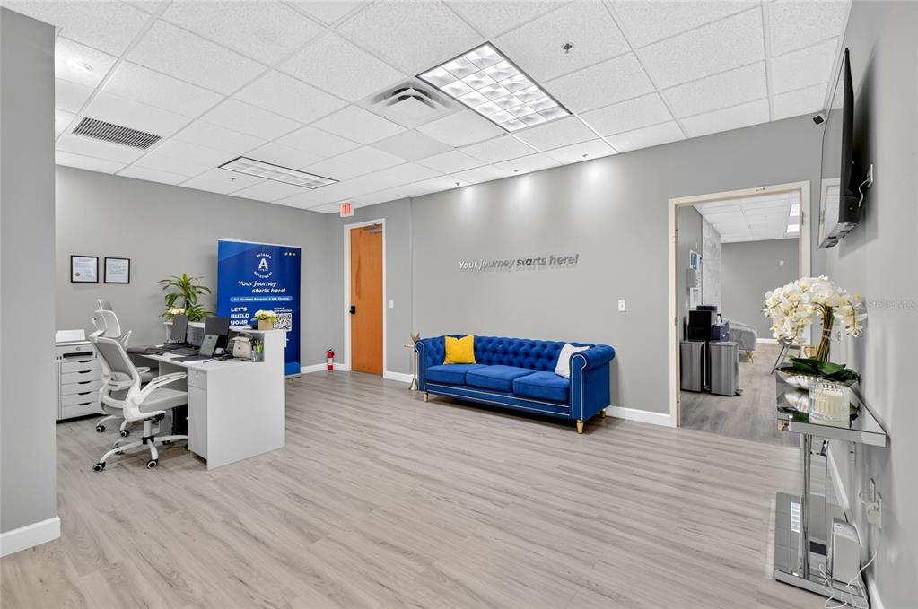 A modern office reception area features a blue tufted sofa, a desk, and gray flooring — 6200 METROWEST BOULEVARD UNIT 205, ORLANDO, FL