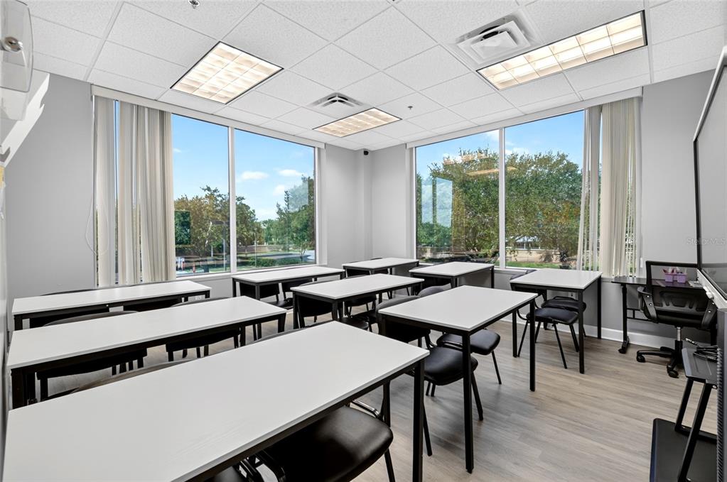 A classroom with white tables, black chairs, large windows, and a drop ceiling — 6200 METROWEST BOULEVARD UNIT 205, ORLANDO, FL