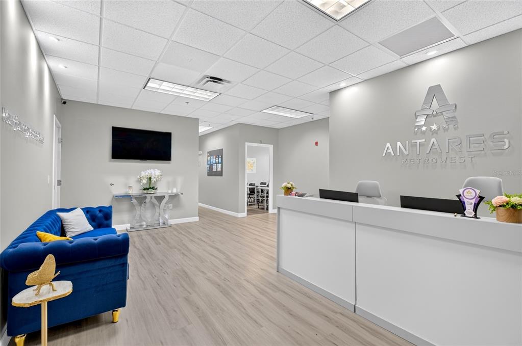 A modern office reception area features a blue tufted sofa and a white front desk — 6200 METROWEST BOULEVARD UNIT 205, ORLANDO, FL