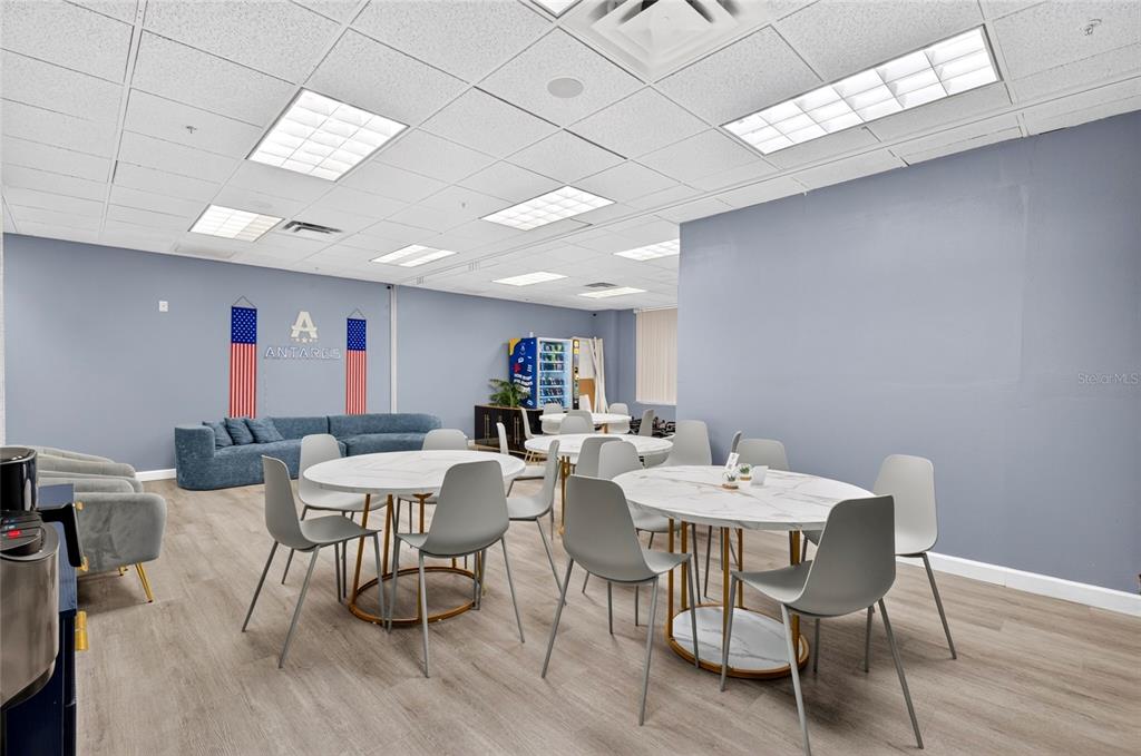 A breakroom features round tables, grey chairs, a blue sofa, and a wall-mounted Antares logo — 6200 METROWEST BOULEVARD UNIT 205, ORLANDO, FL