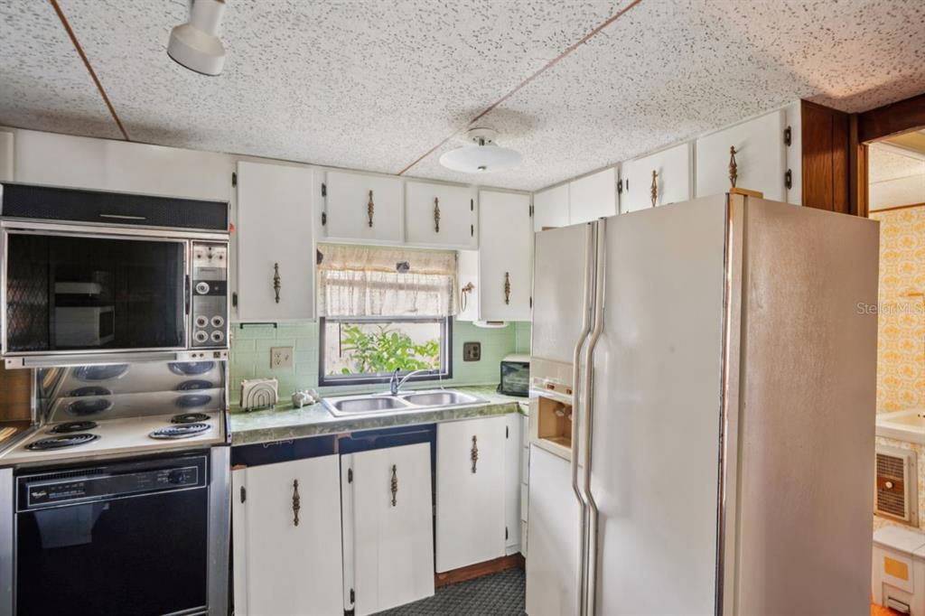 A kitchen features white cabinets, a double sink, a black oven, and a white refrigerator — 9310 KIOWA DR, NEW PORT RICHEY, FL