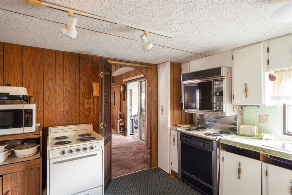 A kitchen with wood-paneled walls, white cabinets, two stoves, and a view into another room — 9310 KIOWA DR, NEW PORT RICHEY, FL