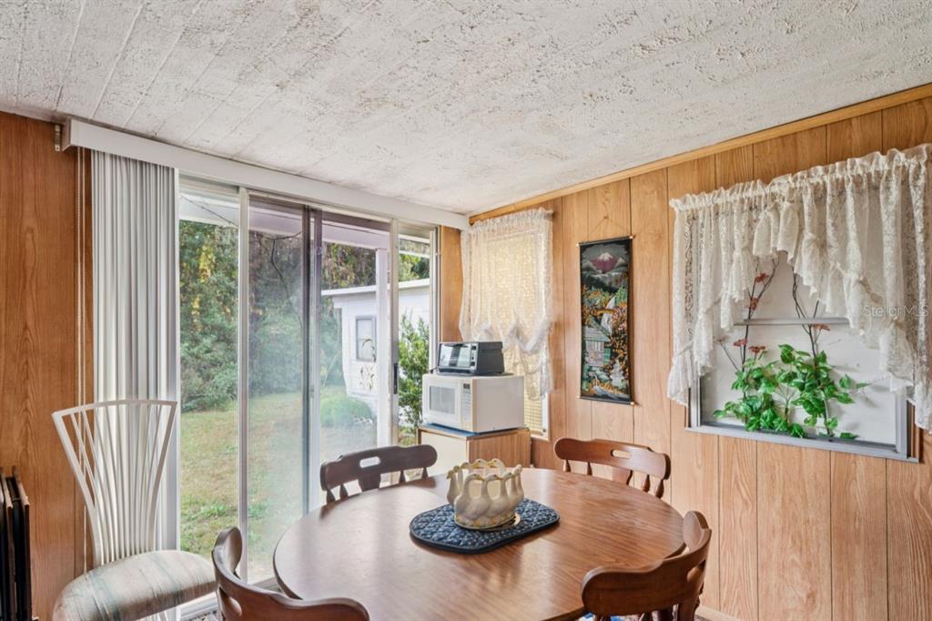 A dining area with wood-paneled walls, a round table, and sliding glass doors to the yard — 9310 KIOWA DR, NEW PORT RICHEY, FL