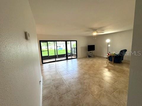 A spacious living room features light tile flooring, a ceiling fan, and large sliding glass doors — 11412 8TH ST N UNIT 1001, ST PETERSBURG, FL
