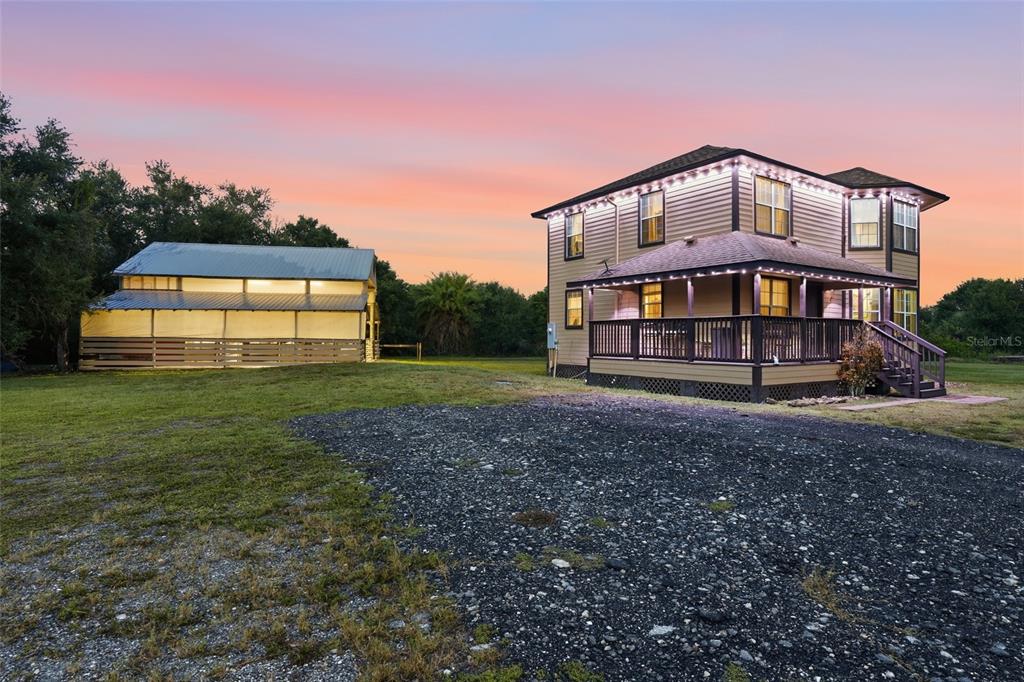 A two-story house with a wrap-around porch stands next to a metal barn at sunset — 5780 SABAL PALM LANE, PUNTA GORDA, FL